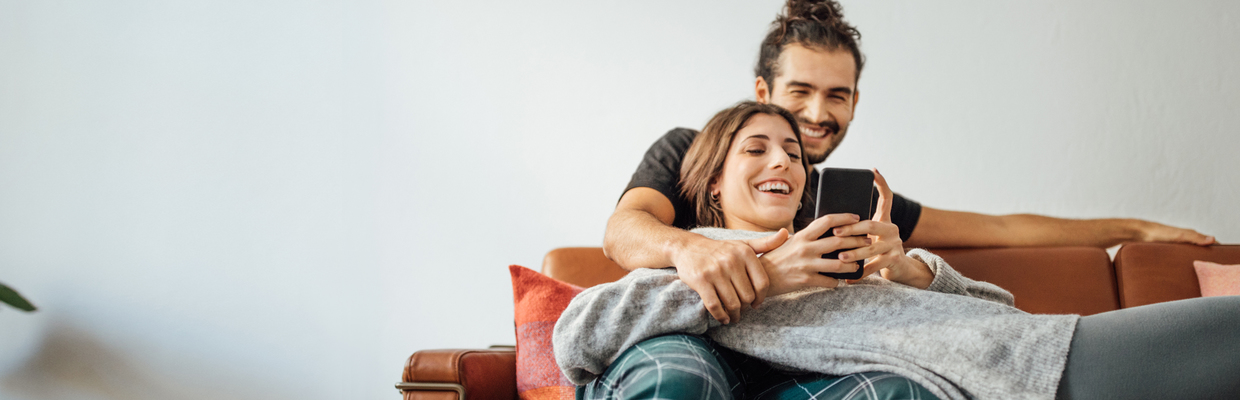 Happy couple reading on mobile phone on couch; image used for HSBC New Zealand Financial Hardship page